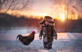 Little boy with a rooster in the snow in winter