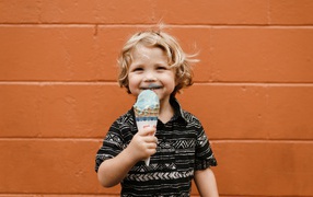 Маленький мальчик с мороженым в руках у стены