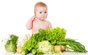 Little child with vegetables and greens on a white background