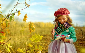 Маленькая девочка рисует красками на листьях осенью 