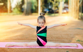 Маленькая девочка гимнастка сидит на шпагате 