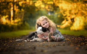 Маленькая девочка обнимает собаку на дороге осенью