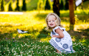 Little girl in a beautiful dress sits on a green grass