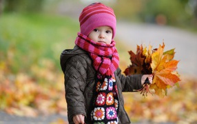 Little girl in a pink hat with leaves in hand