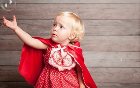 Маленькая девочка в красном платье ловит мыльный пузырь