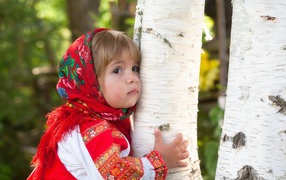 Маленькая девочка в красном платке обнимает березу