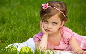 Маленькая девочка в розовом платье лежит на зеленой траве
