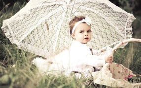 Маленькая девочка сидит на траве с большим белым зонтом