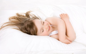 Маленькая девочка спит на белой кровати