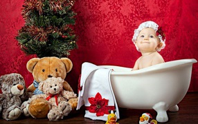 Little girl sitting in a white bath near the Christmas tree with toys