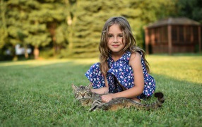 Little girl sitting on the green grass with a gray cat  