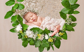 Маленькая девочка спит в колыбеле украшенной зелеными листьями