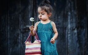 Маленькая девочка с сумкой и одуванчиком в руке