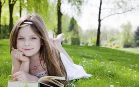 Маленькая девочка с книгой лежит на зеленой траве