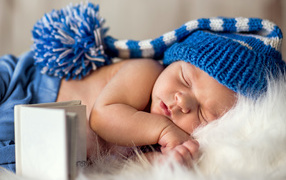 Маленький спящий грудной ребенок в синей вязанной шапке 