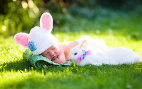 Little sleeping baby on green grass with white rabbit