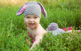 Little smiling baby in a bunny suit lying in the green grass