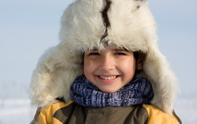 Маленький улыбающийся мальчик в теплой шапке зимой