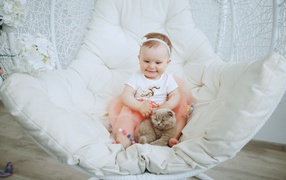 Маленький улыбающийся ребенок с котом сидит в белом кресле