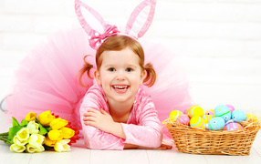 Little smiling girl in pink with Easter eggs and a bouquet of tulips