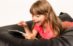 Маленькая улыбающаяся девочка лежит с планшетом