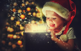 Маленькая улыбающаяся девочка открывает подарок у новогодней елки 