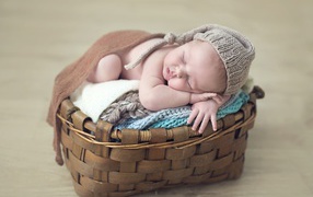Спящий грудной ребенок в шапке в корзине 