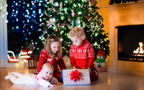 Маленькие дети с новогодним подарком у наряженной елки