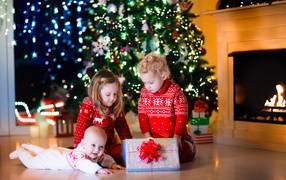 Маленькие дети с новогодним подарком у наряженной елки