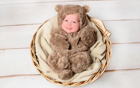 Улыбающийся грудной ребенок в костюме мишки лежит в корзине