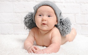 Улыбающийся грудной ребенок в серой шапке с бубонами
