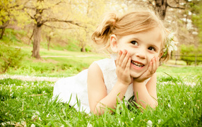 Улыбающаяся девочка в белом платье лежит на зеленой траве