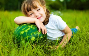 Улыбающаяся девочка с зеленым арбузом на траве