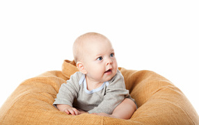 Младенец сидит на подушке на белом фоне