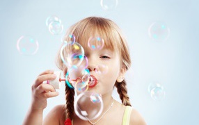 Девочка с косичками пускает мыльные пузыри