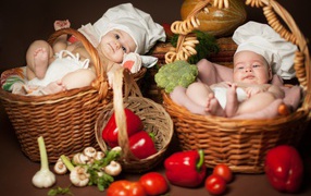 Два младенца в шапках повара лежат в корзинах с продуктами