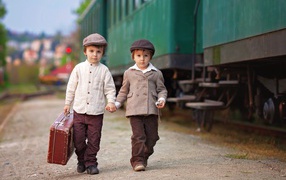 Два маленьких мальчика с большим чемоданом у поезда
