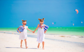 Две маленькие девочки идут по песку