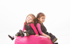 Two little girls sitting on a red soft ball