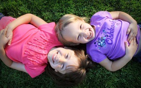 Two little smiling girls lie on the green grass