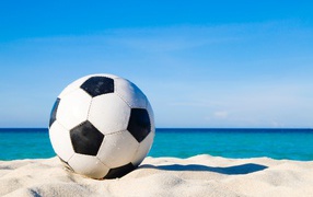 Soccer ball on white sand on a background of blue sky
