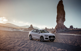 Внедорожник Audi Q8 стоит на песке на фоне скалы 