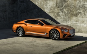 Оранжевый автомобиль Bentley Continental GT V8, 2019 года на фоне стены