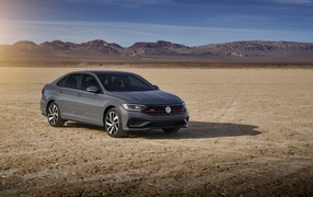 Серебристый автомобиль Volkswagen Jetta на фоне гор под голубым небом