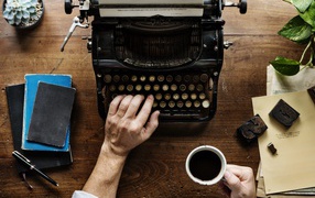 Мужчина с чашкой кофе в руке печатает на старой печатной машинке 