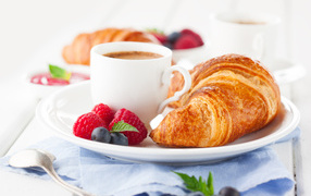 A cup of coffee on a plate with croissant and berries