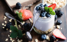A jar of cereal, yogurt and berries on the table with spoons
