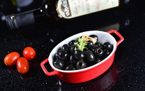 Black olives on the table with a bottle and tomatoes