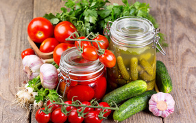 Консервированные помидоры и огурцы на столе со свежими овощами и зеленью 