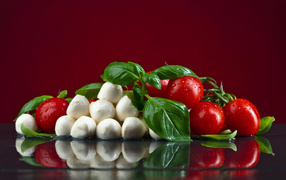 Сыр на столе с зеленью базилика и красными помидорами